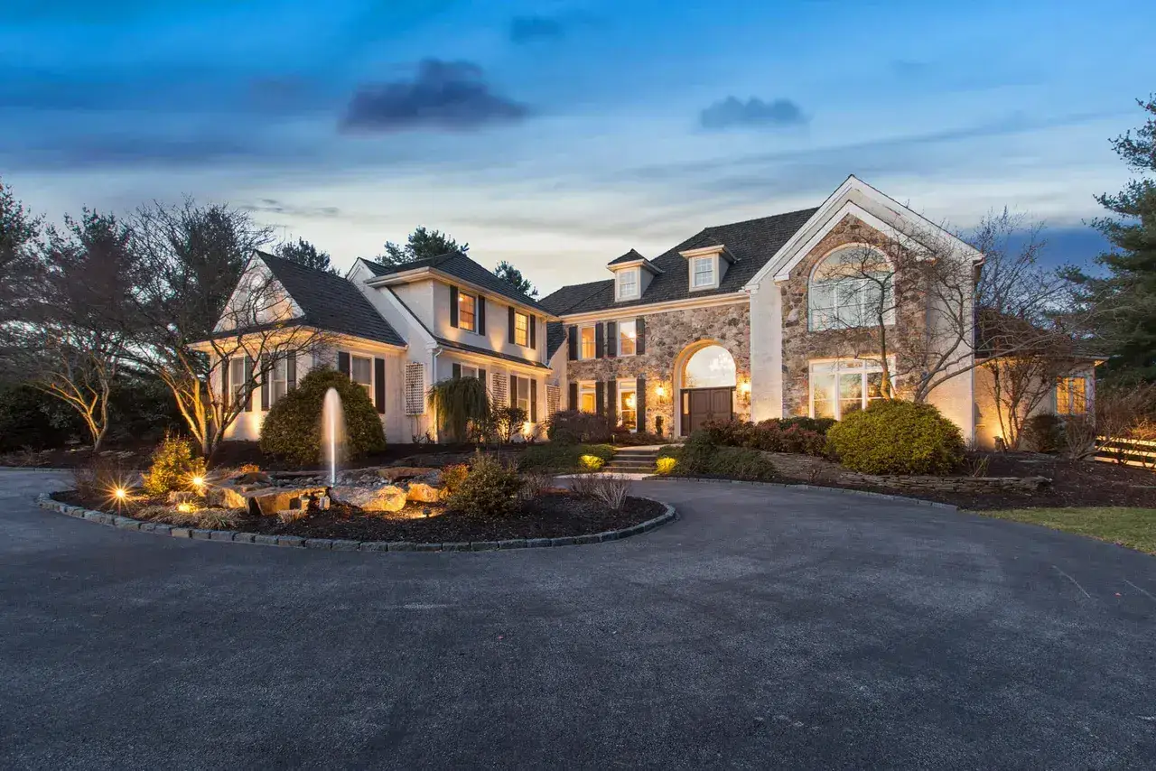 Stone-front home at twilight with illuminated windows and garden lighting