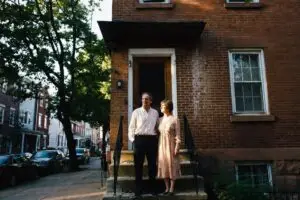 how to sell a house without a realtor in pennsylvania - couple standing on the front stoop of a Philadelphia brick rowhouse on a tree-lined street