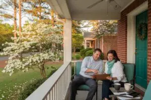 how much are closing costs in nc - couple reviewing home sale paperwork on the porch of a brick ranch house in Charlotte North Carolina